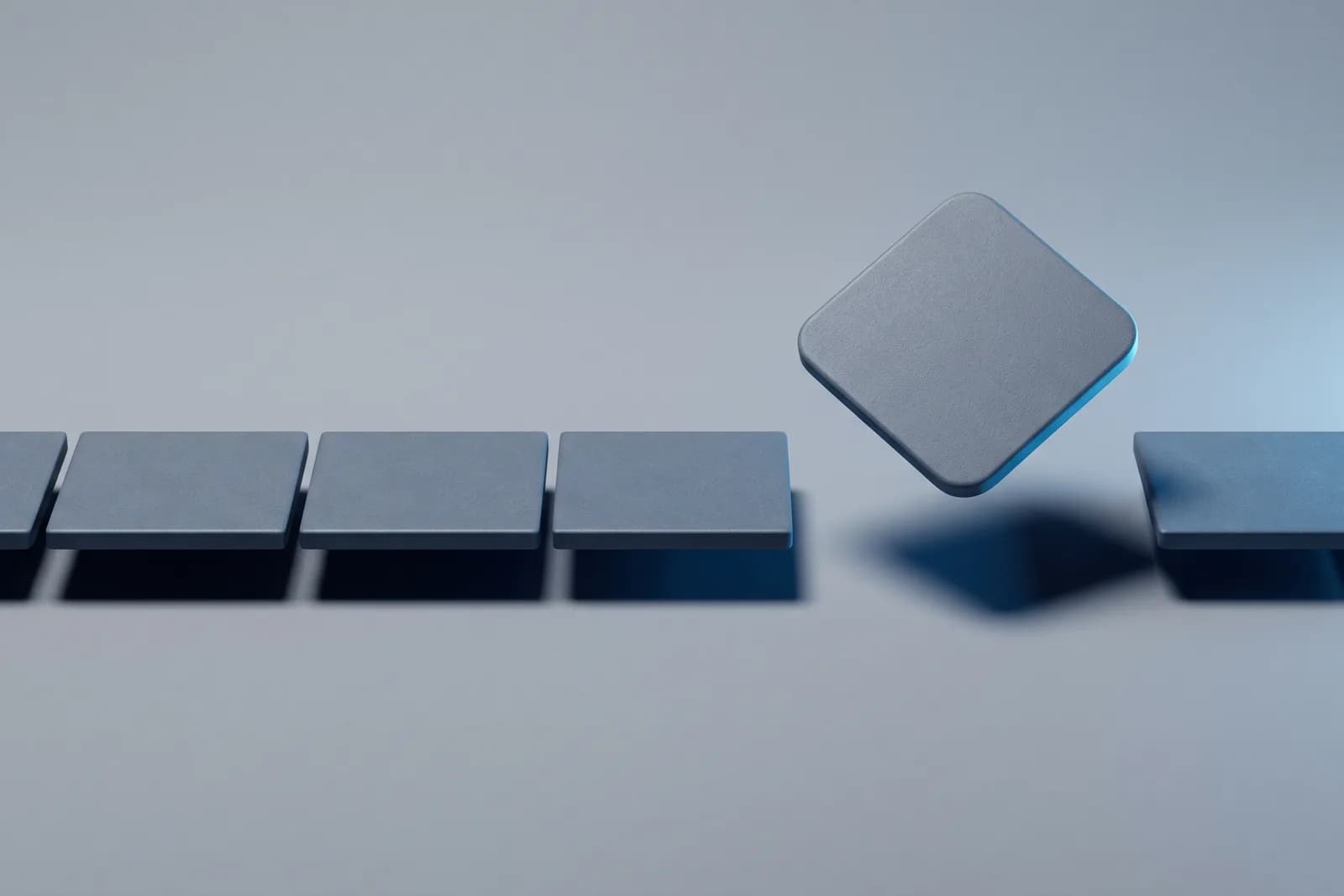 A row of matte slate tiles on cool grey with one rounded-diamond tile lifted out of the gap it left.