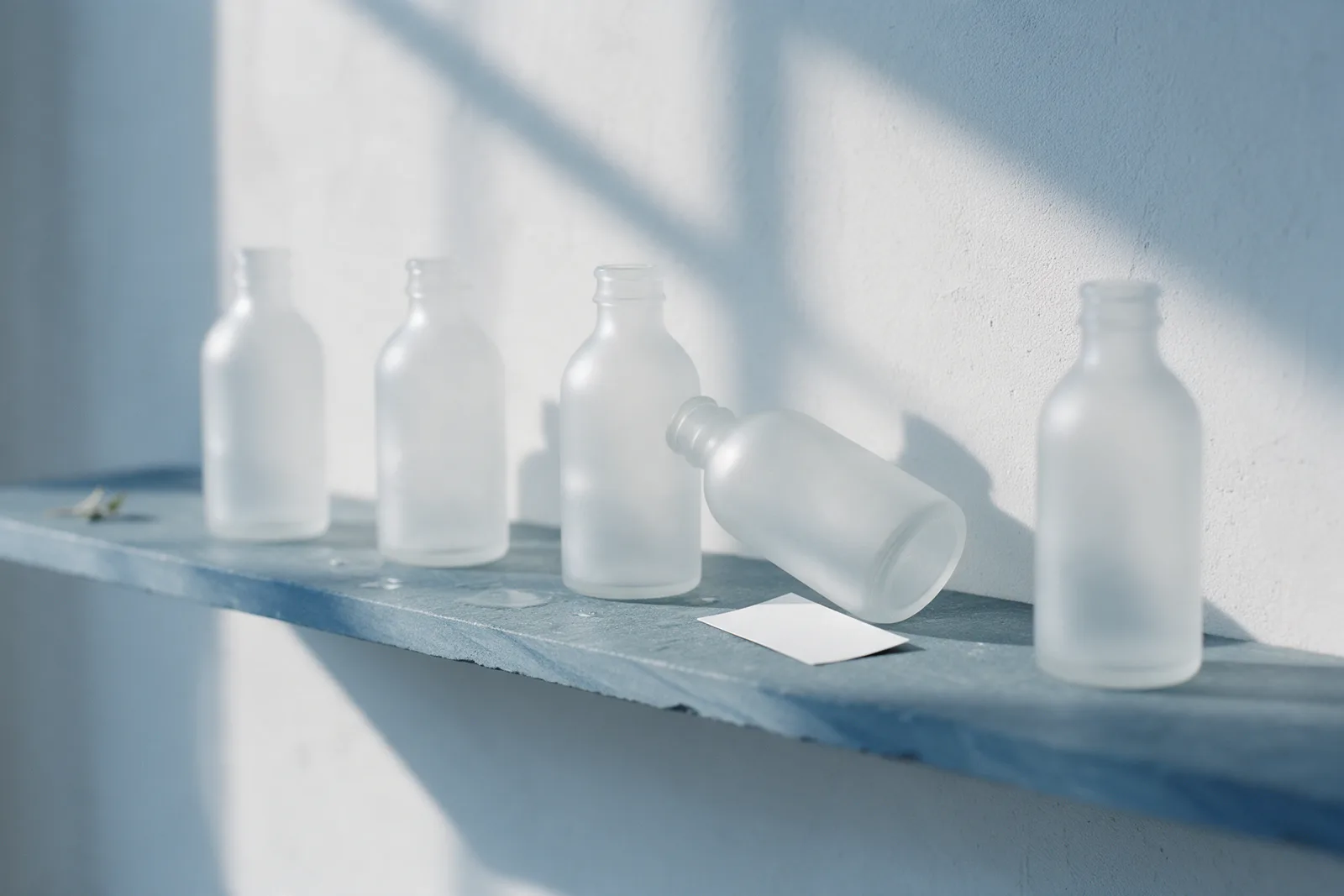 A row of frosted bottles on a slate shelf with one bottle tipped on its side and a blank card fallen beside it.