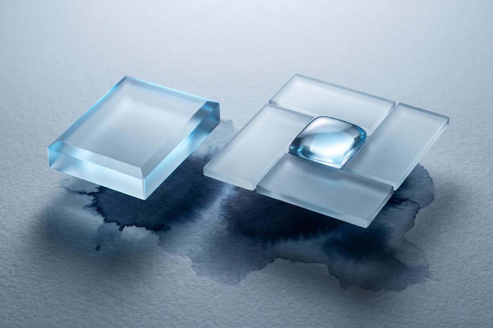 A single frosted glass block beside a wider cluster of linked frosted tiles holding a clear rounded form, over navy ink.