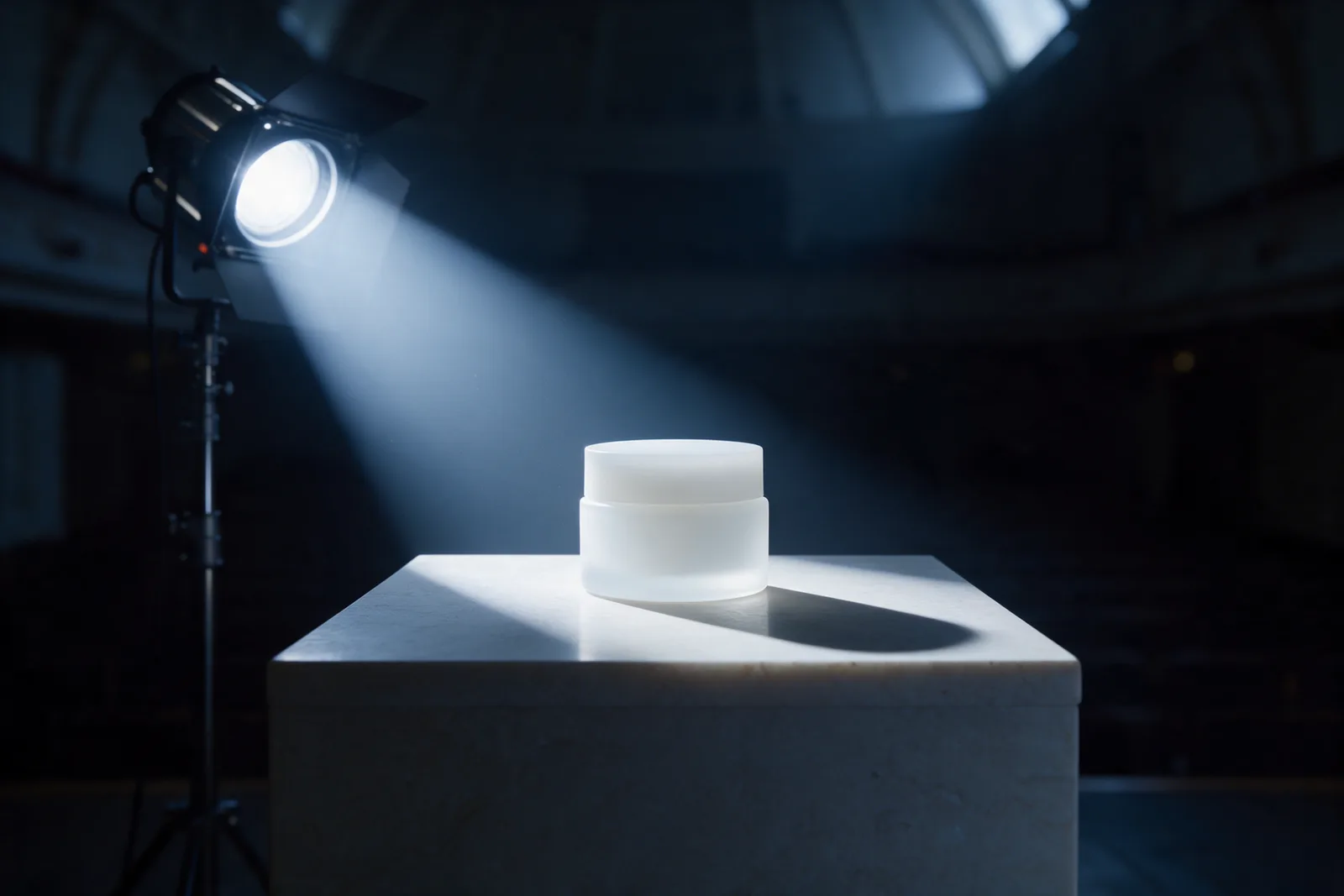 A stage light beams across a dark hall onto one unlabelled white jar on a pale stone plinth.