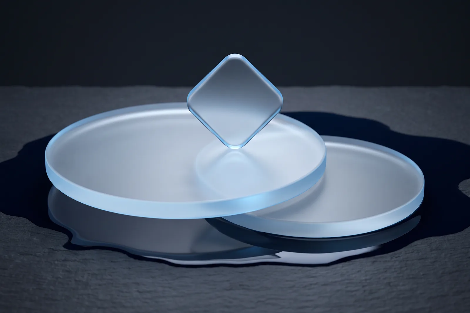 Two interlocking frosted glass discs on dark slate with a rounded frosted tile standing on its point where they meet.