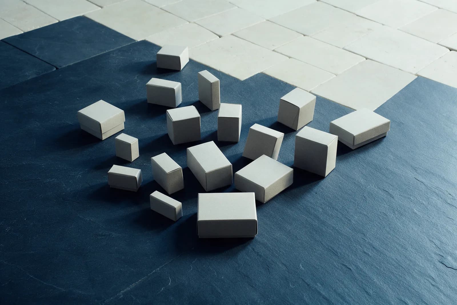 Small unlabelled white boxes fanned across a navy slate table, pale stone tiles laid in a grid behind.